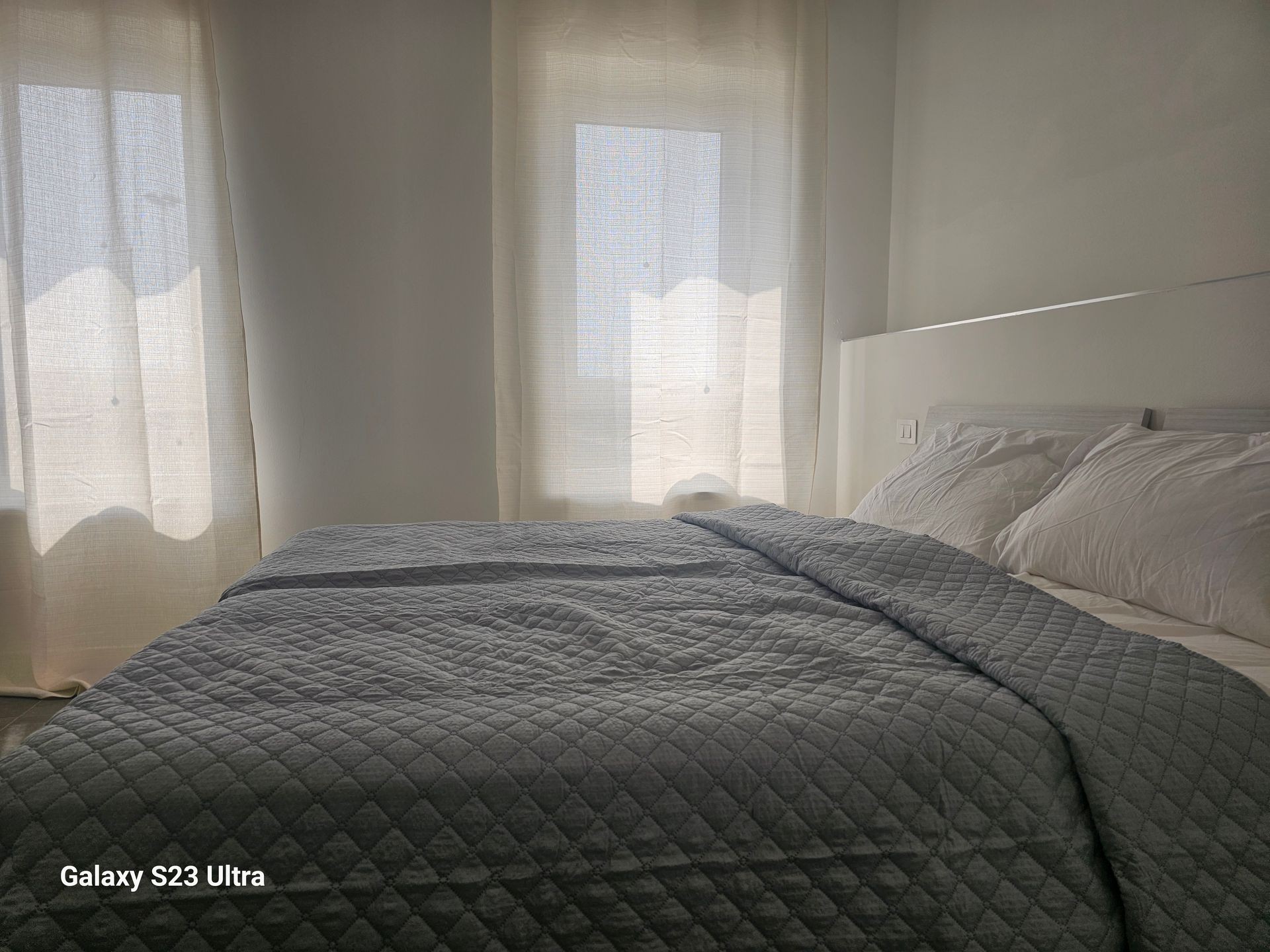 Minimalist bedroom with a neatly made bed and light streaming through sheer curtains.