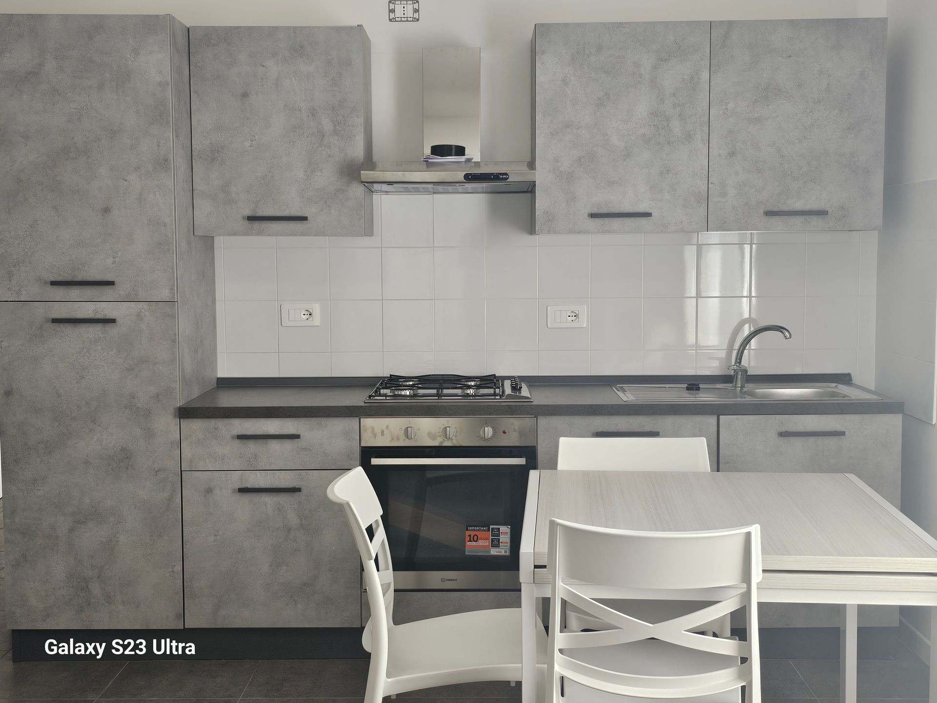 Modern kitchen with gray cabinets, stove, sink, and small dining table with chairs.