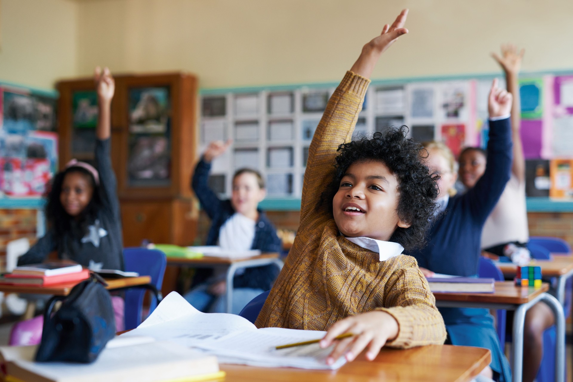 Shot of a diverse group of children sitting in their school classroom and raising their hands to answer a question
