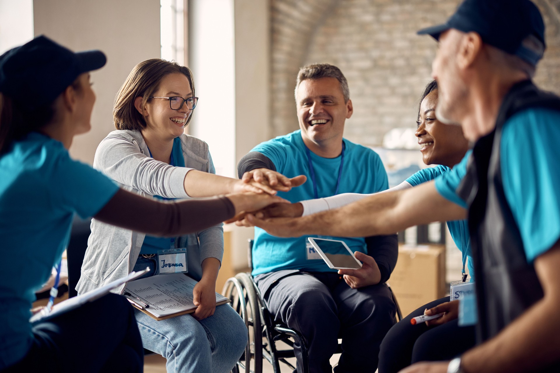 Multiracial group of happy volunteers stacking their hands in unity while working at humanitarian aid center.